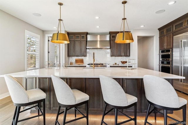 kitchen featuring wall chimney range hood, a breakfast bar, dark brown cabinets, stainless steel appliances, and a spacious island