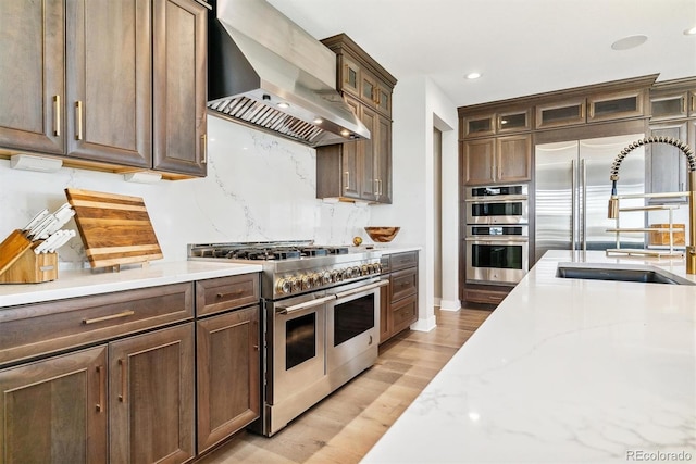 kitchen with wall chimney range hood, sink, appliances with stainless steel finishes, backsplash, and light stone countertops