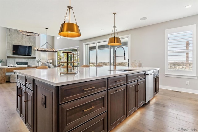 kitchen with sink, dark brown cabinets, an island with sink, pendant lighting, and light hardwood / wood-style floors