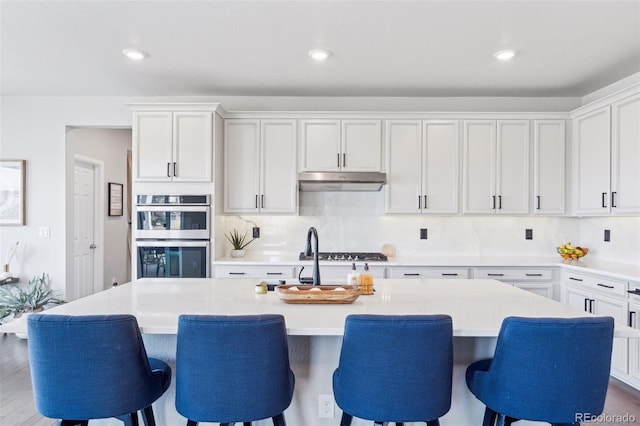 kitchen featuring light countertops, stainless steel appliances, a kitchen island with sink, and under cabinet range hood