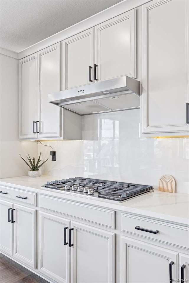 kitchen with light stone counters, under cabinet range hood, stainless steel gas cooktop, white cabinetry, and tasteful backsplash