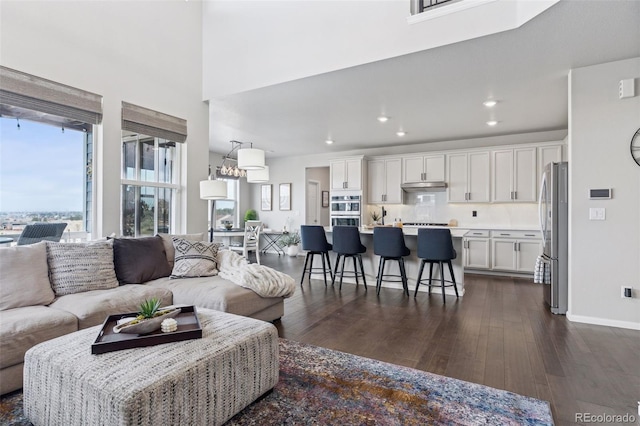 living room featuring a towering ceiling, baseboards, dark wood-type flooring, and recessed lighting