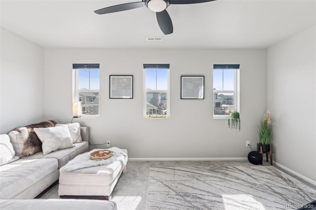 living area featuring baseboards, visible vents, a ceiling fan, and light colored carpet