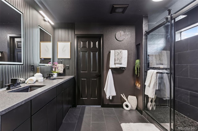 bathroom with a stall shower, double vanity, a sink, and tile patterned floors