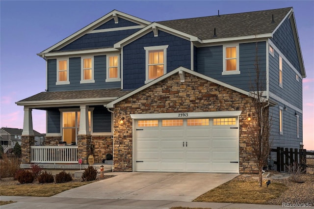 craftsman-style house featuring covered porch, driveway, stone siding, and an attached garage