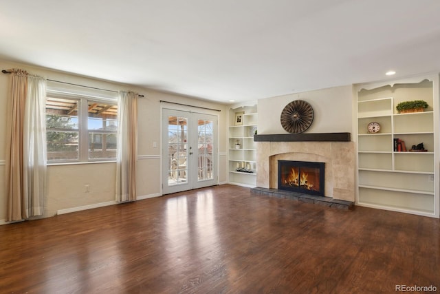 unfurnished living room featuring built in shelves, baseboards, a tile fireplace, french doors, and wood finished floors