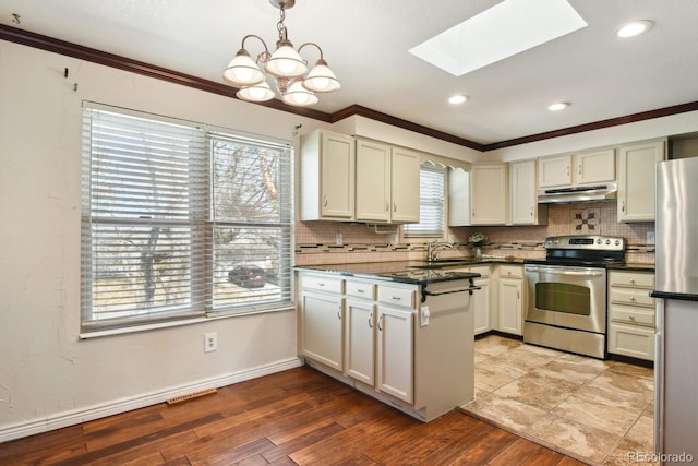 kitchen with dark countertops, under cabinet range hood, ornamental molding, stainless steel appliances, and a sink