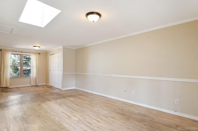 spare room featuring light wood finished floors, a skylight, crown molding, and baseboards