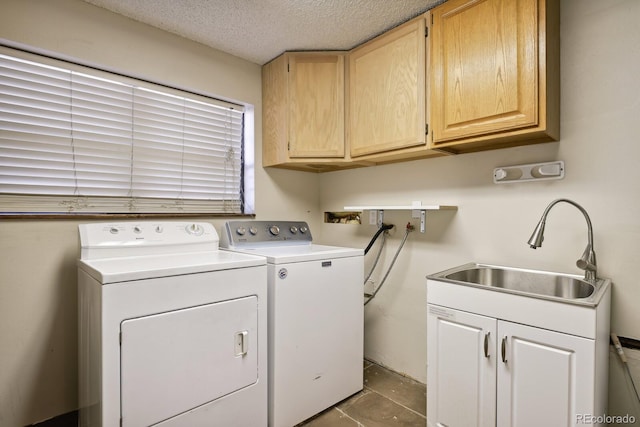 clothes washing area with a textured ceiling, washer and clothes dryer, cabinet space, and a sink