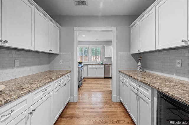 1366 S Vine St, Denver, CO 80210 - kitchen featuring appliances with stainless steel finishes, wine cooler, a sink, white cabinetry, and light wood-type flooring
