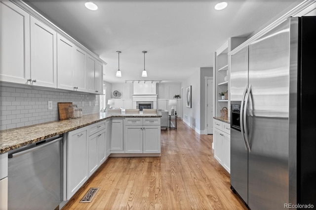 1366 S Vine St, Denver, CO 80210 - kitchen featuring stainless steel appliances, light wood-style flooring, decorative backsplash, white cabinets, and a peninsula