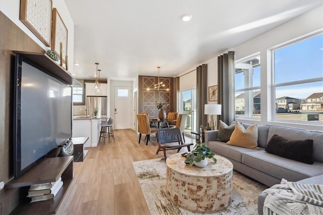 living room featuring sink, light hardwood / wood-style flooring, and a notable chandelier