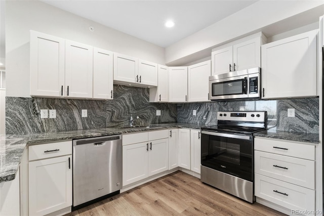875 E 78th Ave Unit 52, Denver, CO 80229 - kitchen with appliances with stainless steel finishes, a sink, white cabinetry, light wood finished floors, and dark stone countertops