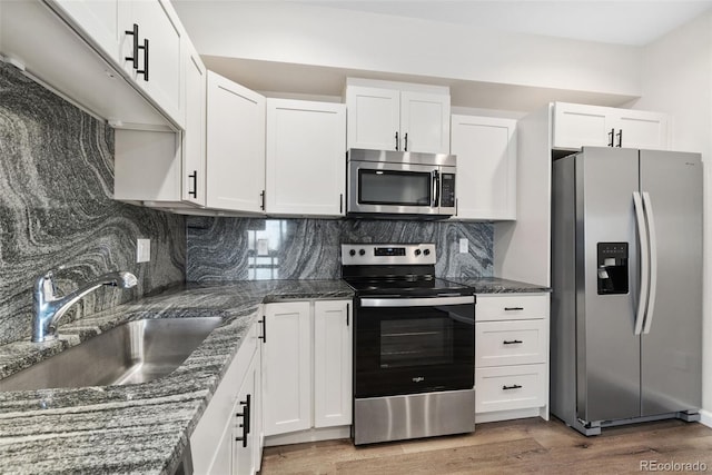 875 E 78th Ave Unit 52, Denver, CO 80229 - kitchen with appliances with stainless steel finishes, a sink, light wood-style floors, white cabinetry, and decorative backsplash