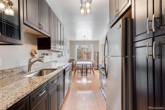 kitchen with appliances with stainless steel finishes, light stone counters, a sink, light wood finished floors, and glass insert cabinets