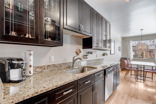 kitchen with light stone countertops, dark brown cabinets, a sink, dishwasher, and light wood-style floors