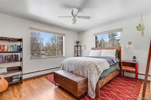 bedroom with ceiling fan, baseboard heating, and wood finished floors