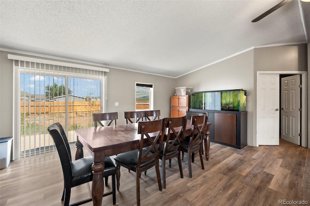 dining space with ceiling fan, crown molding, hardwood / wood-style floors, vaulted ceiling, and a textured ceiling