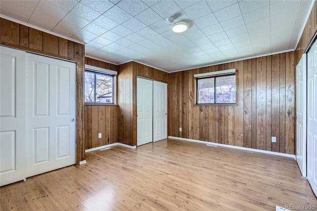 unfurnished bedroom featuring light hardwood / wood-style flooring, ornamental molding, and wooden walls