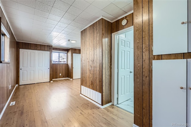 corridor with crown molding, light wood-type flooring, and wood walls