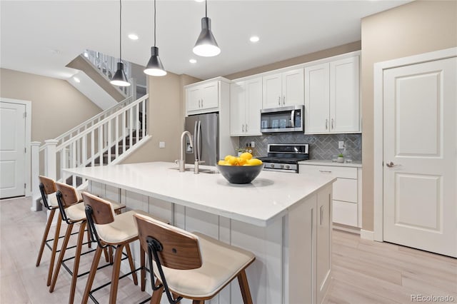 239 W Jamison Ct, Littleton, CO 80120 - kitchen featuring appliances with stainless steel finishes, white cabinetry, backsplash, a kitchen island with sink, and a breakfast bar