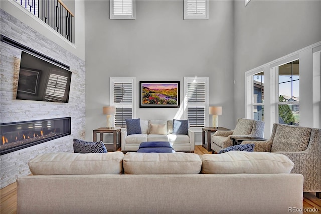 living area with a stone fireplace, a towering ceiling, and wood finished floors
