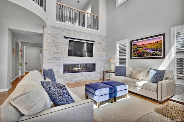 living area featuring a glass covered fireplace, baseboards, a high ceiling, and wood finished floors