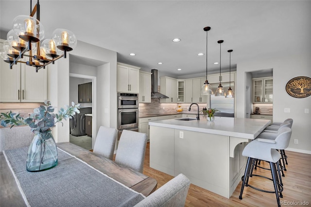 kitchen with light wood-type flooring, a sink, stainless steel appliances, recessed lighting, and wall chimney exhaust hood