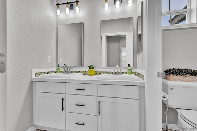 full bathroom featuring a sink, baseboards, toilet, and double vanity