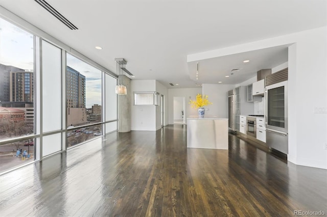 kitchen with a wall of windows, stainless steel appliances, dark hardwood / wood-style floors, white cabinets, and decorative light fixtures