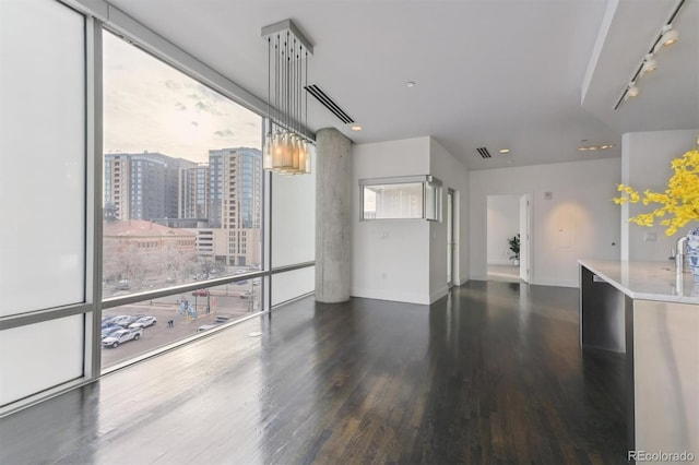 unfurnished living room with visible vents, wood finished floors, a wall of windows, baseboards, and rail lighting