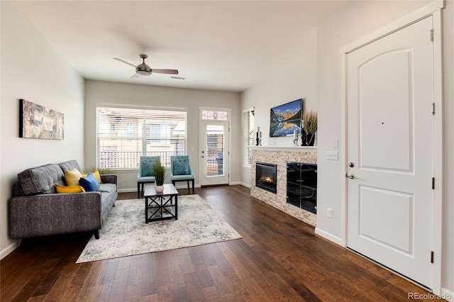 living room featuring dark wood-type flooring, ceiling fan, and a stone fireplace