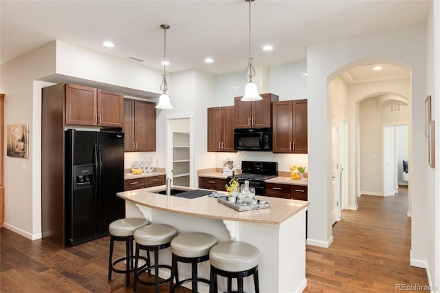 kitchen with dark hardwood / wood-style floors, a kitchen breakfast bar, pendant lighting, a kitchen island with sink, and black appliances