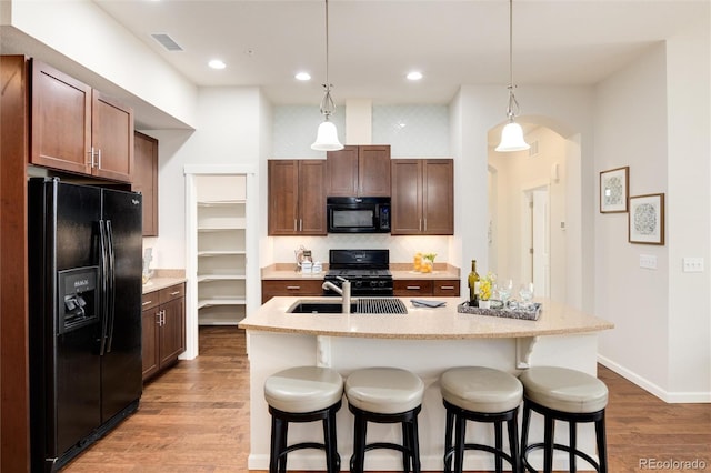 kitchen with a breakfast bar, hanging light fixtures, a center island with sink, and black appliances