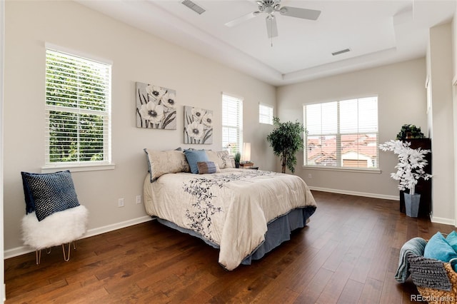 bedroom with a raised ceiling, dark wood-type flooring, and ceiling fan