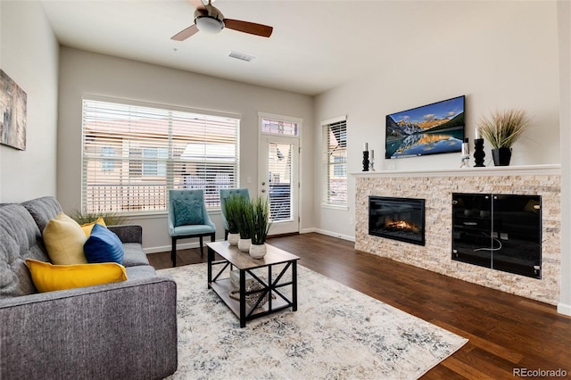 living room featuring ceiling fan, wood-type flooring, and a stone fireplace