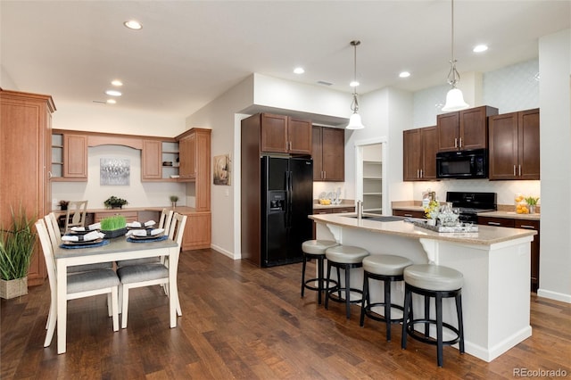 kitchen with dark wood-type flooring, sink, an island with sink, pendant lighting, and black appliances