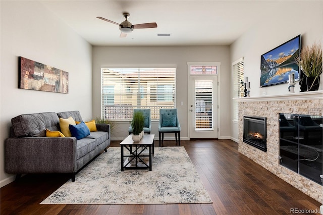 living room with a stone fireplace, dark hardwood / wood-style floors, and ceiling fan