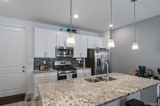 kitchen featuring stainless steel appliances, a sink, white cabinetry, light wood-style floors, and decorative backsplash