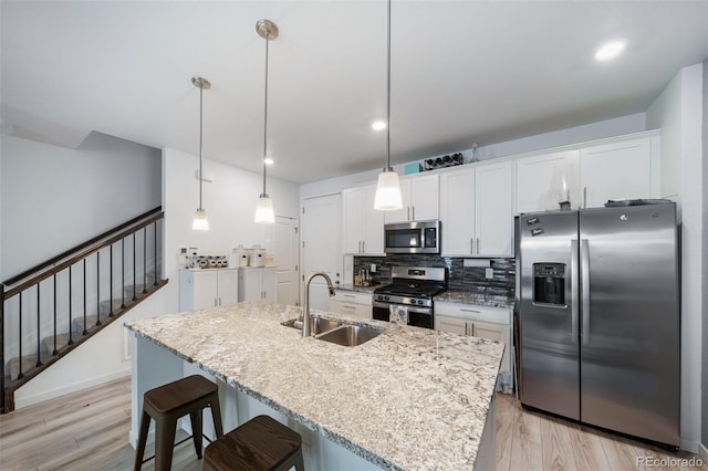 kitchen featuring tasteful backsplash, white cabinets, stainless steel appliances, light wood-type flooring, and a sink