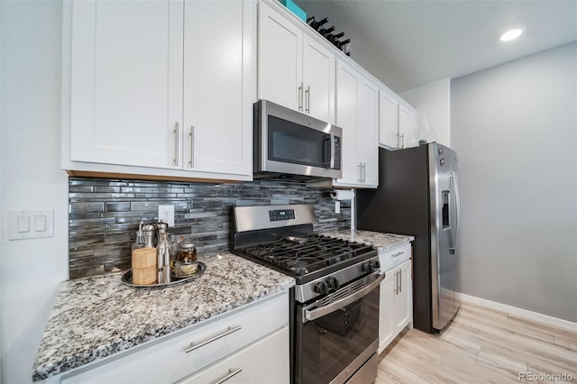 kitchen featuring appliances with stainless steel finishes, white cabinetry, light stone counters, and tasteful backsplash