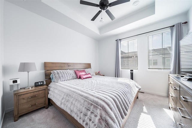 bedroom featuring ceiling fan, a tray ceiling, light colored carpet, and baseboards