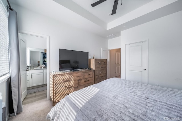 bedroom featuring light carpet, multiple windows, ensuite bath, and a ceiling fan