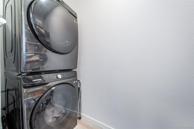 clothes washing area featuring stacked washer and dryer, light wood-style flooring, laundry area, and baseboards