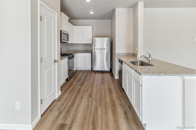 kitchen with appliances with stainless steel finishes, a sink, a peninsula, light wood-style floors, and recessed lighting