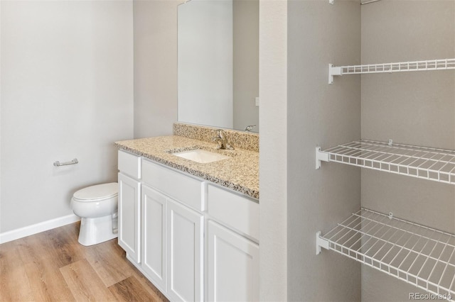 half bath featuring toilet, wood finished floors, vanity, and baseboards