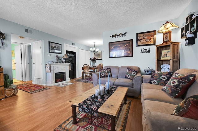 living area with a notable chandelier, a textured ceiling, visible vents, and wood finished floors