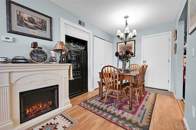 dining area with light wood finished floors, visible vents, a lit fireplace, a notable chandelier, and a textured ceiling