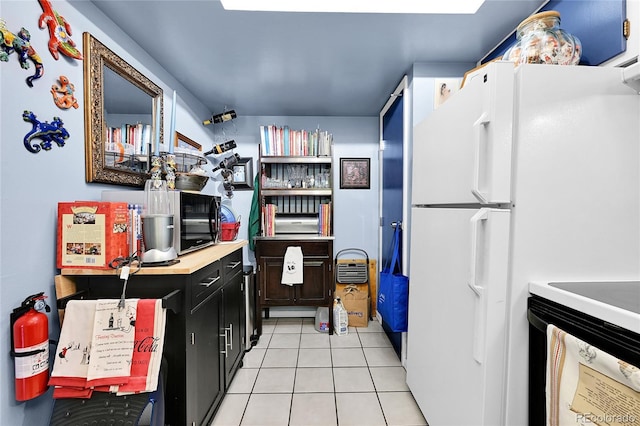 kitchen with light tile patterned flooring, light countertops, freestanding refrigerator, and dark cabinets