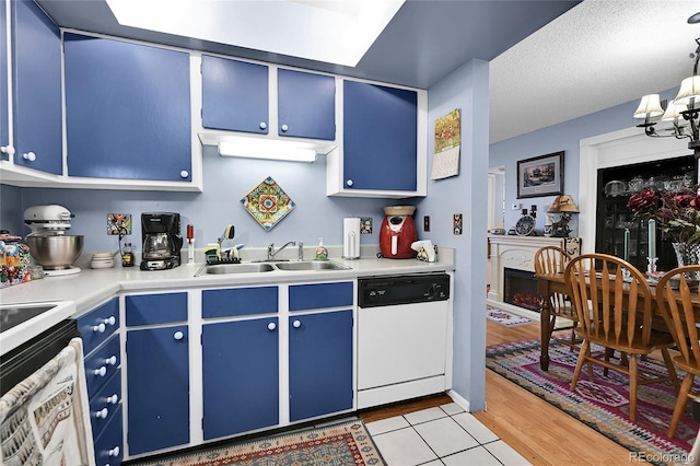 kitchen with a sink, blue cabinetry, a fireplace, white dishwasher, and light countertops